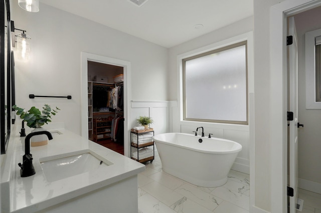 full bathroom with a walk in closet, marble finish floor, a wainscoted wall, a sink, and a freestanding tub