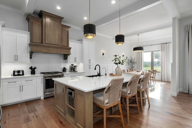 kitchen featuring a center island with sink, stainless steel gas stove, a sink, wood finished floors, and a kitchen breakfast bar