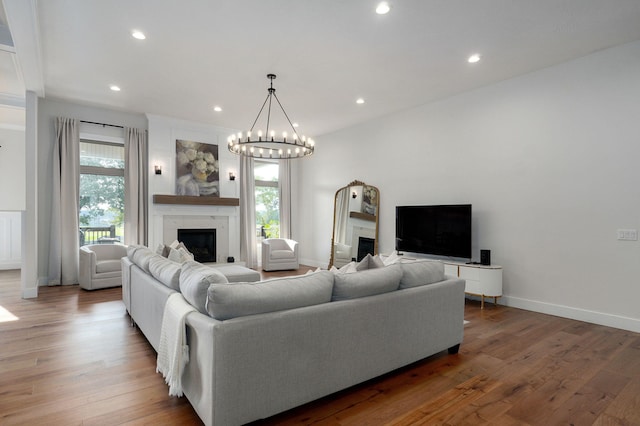 living room featuring a chandelier, recessed lighting, wood finished floors, baseboards, and a glass covered fireplace