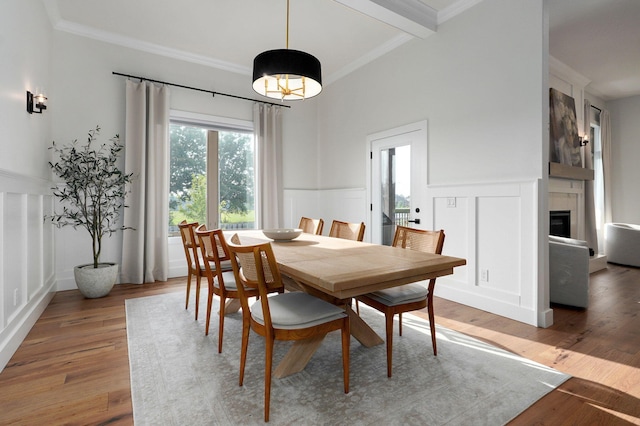 dining space with a fireplace, a decorative wall, light wood-style flooring, ornamental molding, and wainscoting