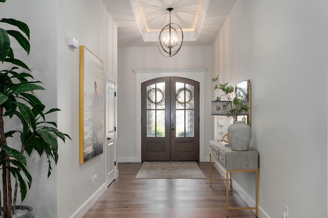 entrance foyer featuring baseboards, wood finished floors, an inviting chandelier, a tray ceiling, and french doors