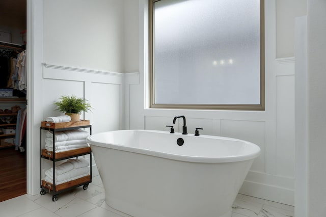 full bathroom featuring plenty of natural light, a soaking tub, marble finish floor, a walk in closet, and a decorative wall