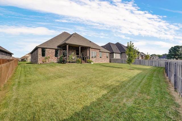 rear view of house featuring brick siding, a yard, and a fenced backyard