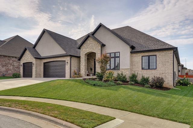 french country home with concrete driveway, roof with shingles, an attached garage, a front yard, and stucco siding