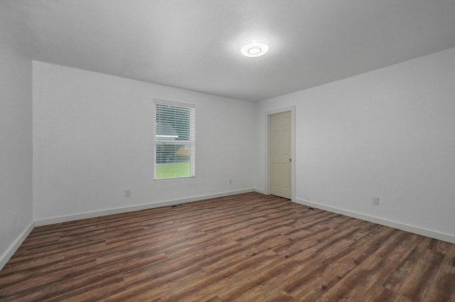 spare room with baseboards and dark wood-style flooring