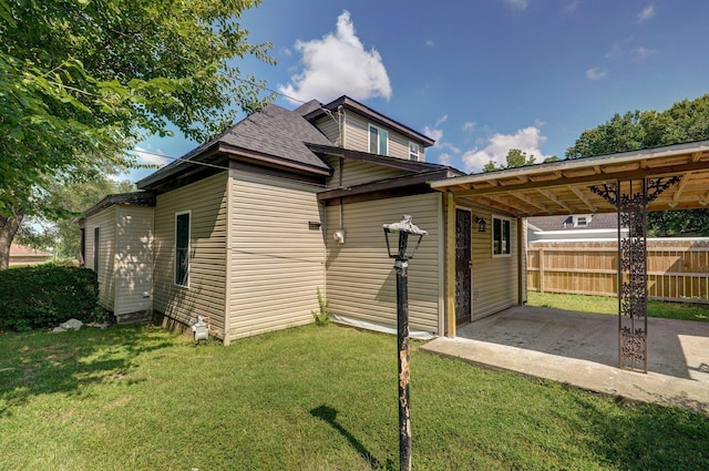 back of property featuring driveway, fence, an attached carport, and a yard