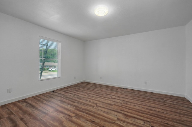 unfurnished room featuring dark wood-style flooring, visible vents, and baseboards