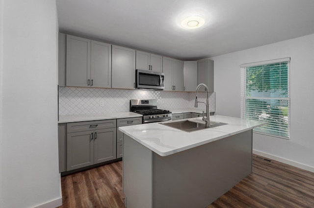 kitchen featuring gray cabinetry, a sink, appliances with stainless steel finishes, decorative backsplash, and dark wood-style floors