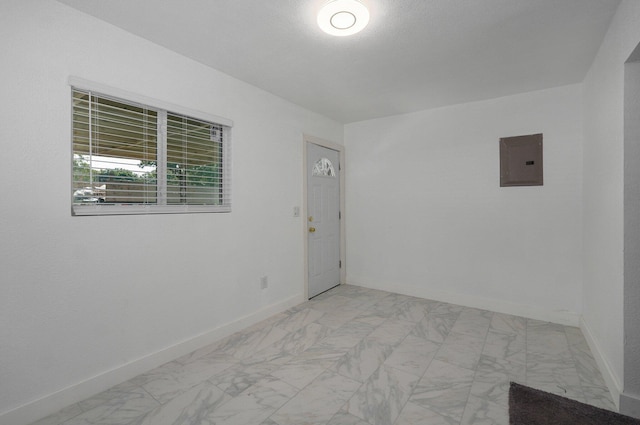 empty room with marble finish floor, electric panel, and baseboards