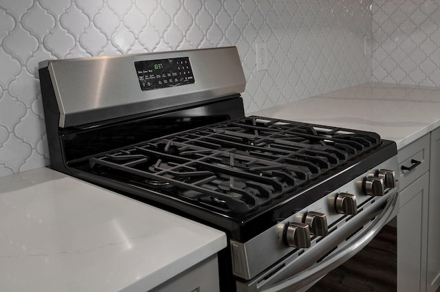 details with gray cabinetry, light countertops, decorative backsplash, and gas range