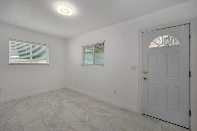 foyer entrance featuring marble finish floor, plenty of natural light, and baseboards