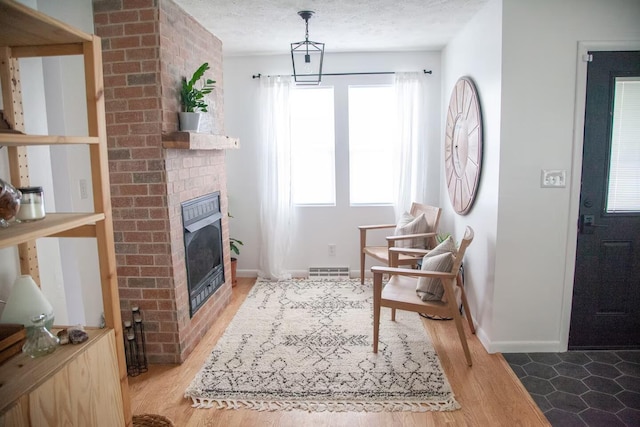 sitting room with a textured ceiling, visible vents, baseboards, light wood-type flooring, and a brick fireplace