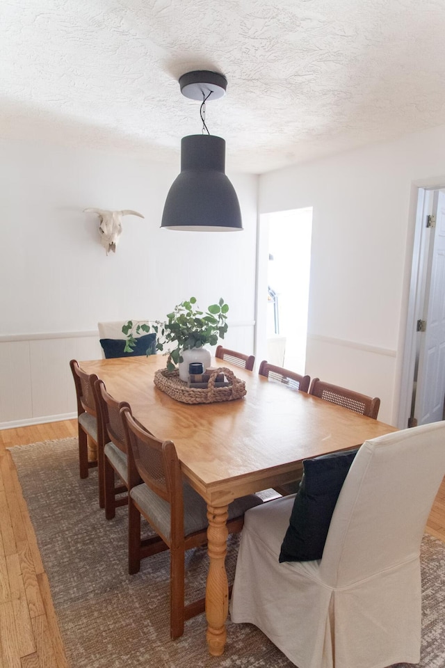 dining space with a wainscoted wall, a textured ceiling, and wood finished floors