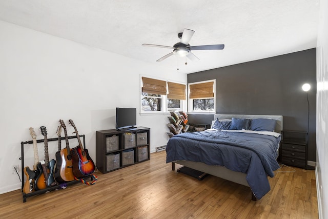 bedroom with a baseboard radiator, wood-type flooring, baseboards, and ceiling fan