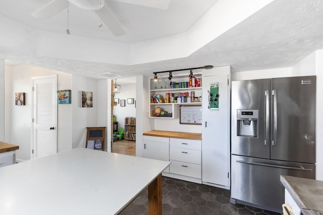 kitchen featuring stainless steel fridge, white cabinetry, wooden counters, and a textured ceiling