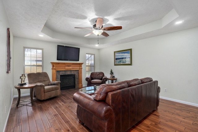 living room featuring hardwood / wood-style flooring, baseboards, a tray ceiling, and a textured ceiling