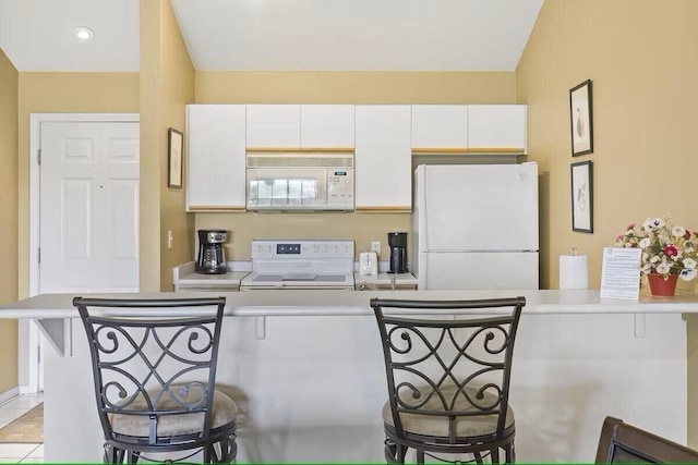 kitchen featuring light countertops, white appliances, a breakfast bar, and white cabinetry