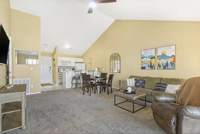 living area with light carpet, visible vents, baseboards, ceiling fan, and high vaulted ceiling