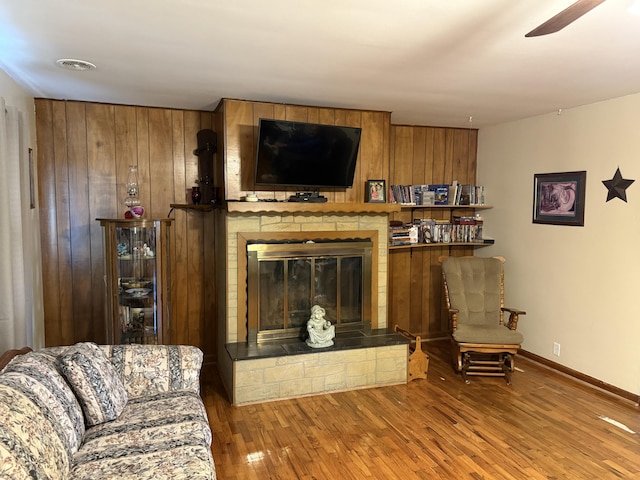 living area with visible vents, a ceiling fan, a large fireplace, wood finished floors, and baseboards