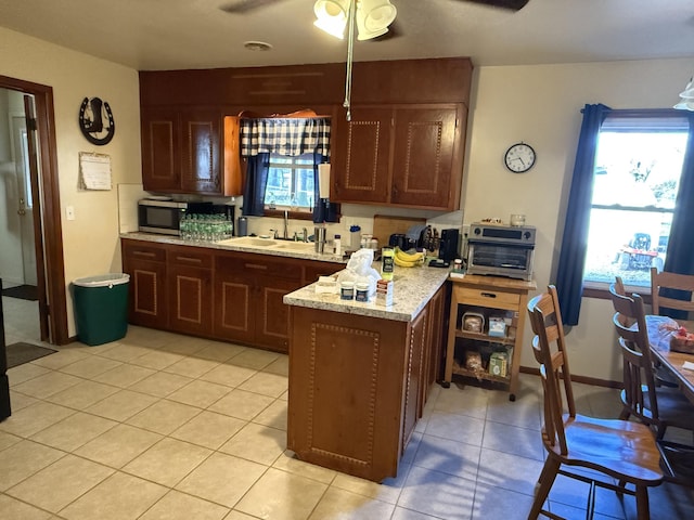 kitchen featuring light tile patterned floors, stainless steel microwave, ceiling fan, a sink, and a peninsula