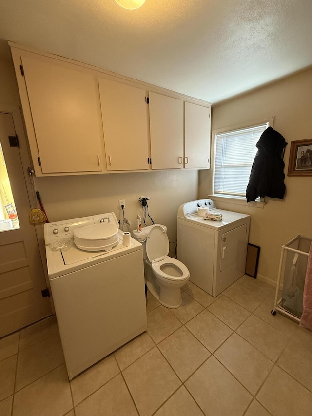 clothes washing area with washer and clothes dryer, a textured ceiling, and light tile patterned flooring