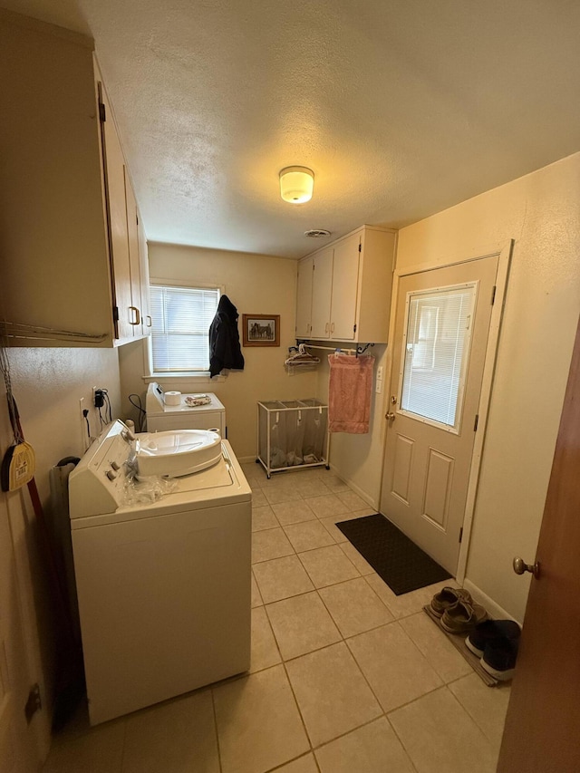 washroom with cabinet space, a textured ceiling, washer and dryer, and light tile patterned flooring