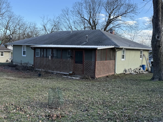 rear view of property with a shingled roof, a sunroom, a yard, and a chimney