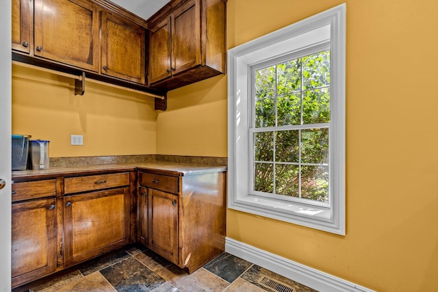 kitchen with dark countertops, plenty of natural light, stone tile flooring, and baseboards