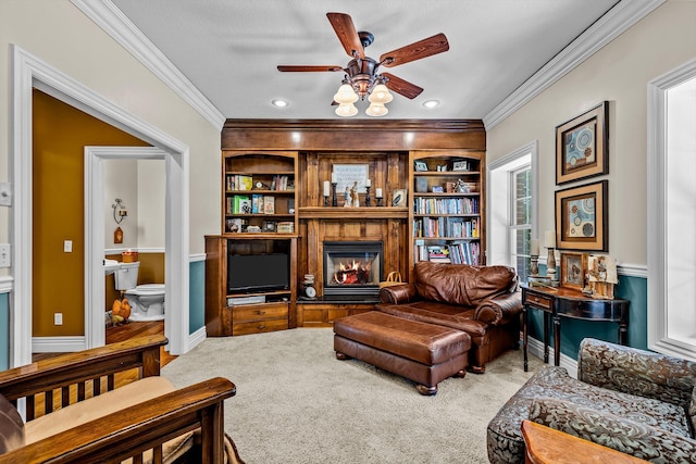 sitting room with carpet floors, a glass covered fireplace, crown molding, and ceiling fan