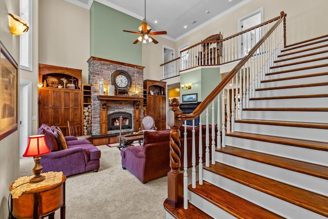 carpeted living area featuring crown molding, stairway, a high ceiling, ceiling fan, and a warm lit fireplace