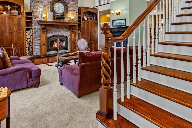 living area featuring carpet, a stone fireplace, a towering ceiling, and stairs