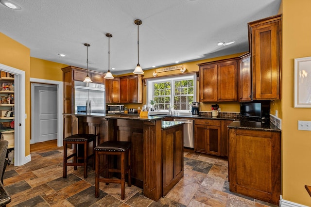 kitchen with a kitchen breakfast bar, appliances with stainless steel finishes, stone finish flooring, dark stone countertops, and decorative light fixtures