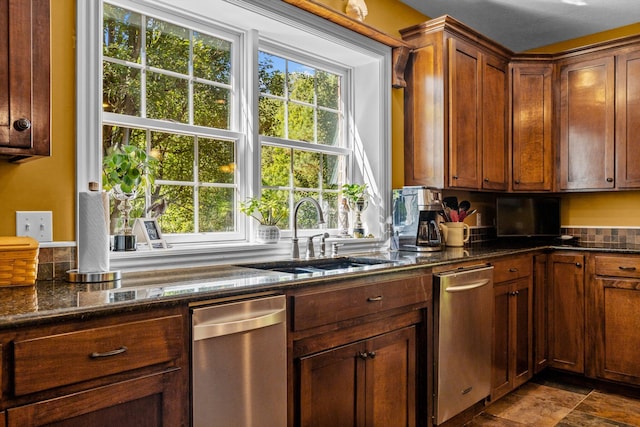 kitchen featuring stone finish flooring, a healthy amount of sunlight, a sink, and dark stone countertops