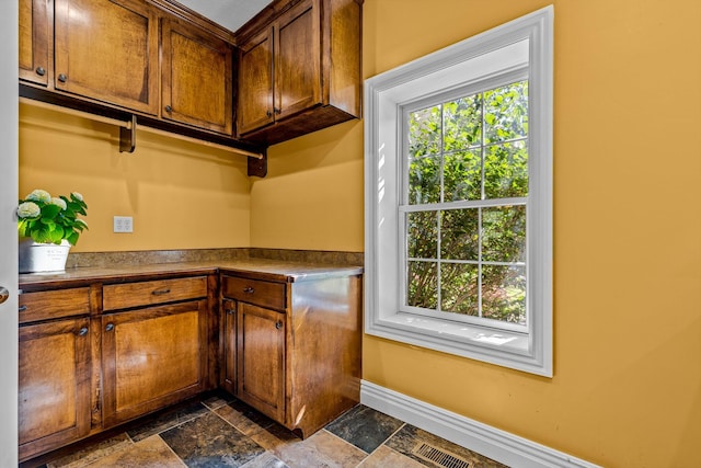 kitchen with a healthy amount of sunlight, dark countertops, stone tile floors, and baseboards