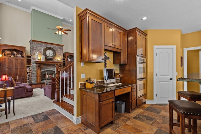 kitchen featuring double oven, a fireplace, baseboards, brown cabinetry, and stone tile flooring