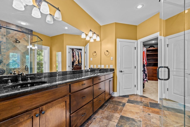 full bathroom with double vanity, a spacious closet, a stall shower, and a sink