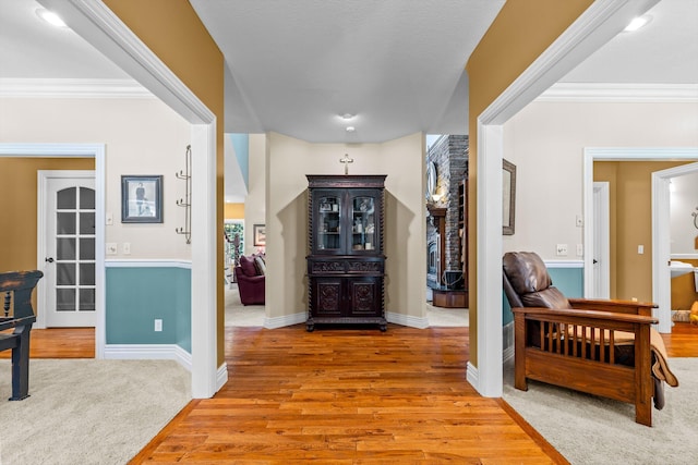 foyer featuring light wood-type flooring, light colored carpet, crown molding, and baseboards