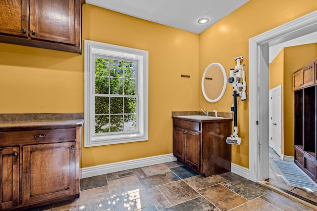 bathroom featuring stone tile flooring, vanity, and baseboards