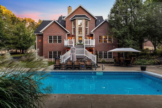 back of property at dusk featuring a patio, a chimney, stairs, a deck, and brick siding