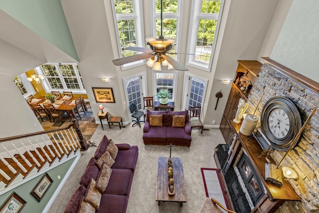 carpeted living room featuring a fireplace with flush hearth, a towering ceiling, baseboards, and ceiling fan with notable chandelier