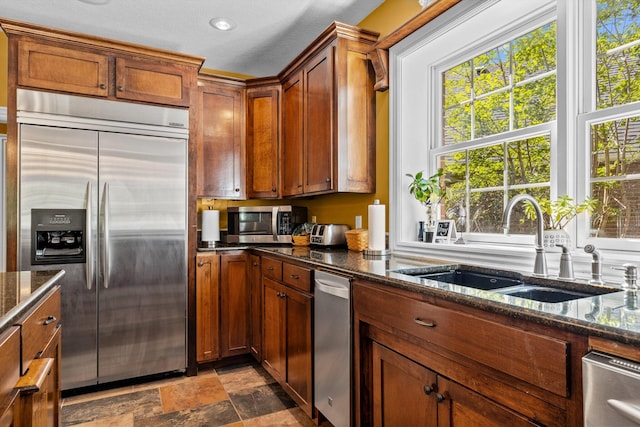 kitchen with stainless steel appliances, stone finish flooring, brown cabinetry, and a sink