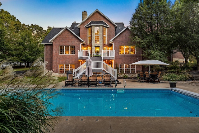 back of house featuring an outdoor pool, a chimney, stairway, a patio area, and brick siding