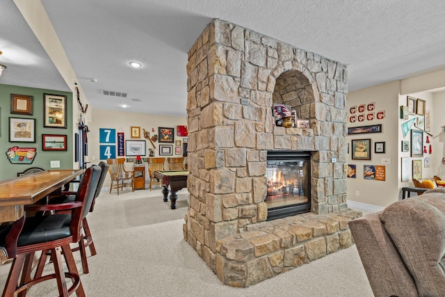 carpeted living room with a textured ceiling, pool table, a stone fireplace, and visible vents