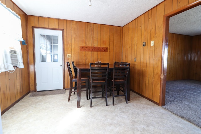 dining area featuring baseboards, light carpet, wooden walls, and a textured ceiling