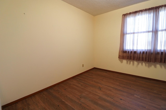 empty room with dark wood-style flooring, a textured ceiling, and baseboards