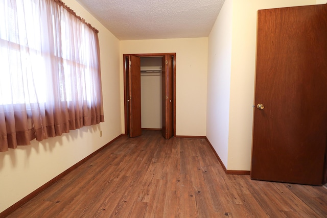 corridor featuring wood-type flooring, baseboards, and a textured ceiling