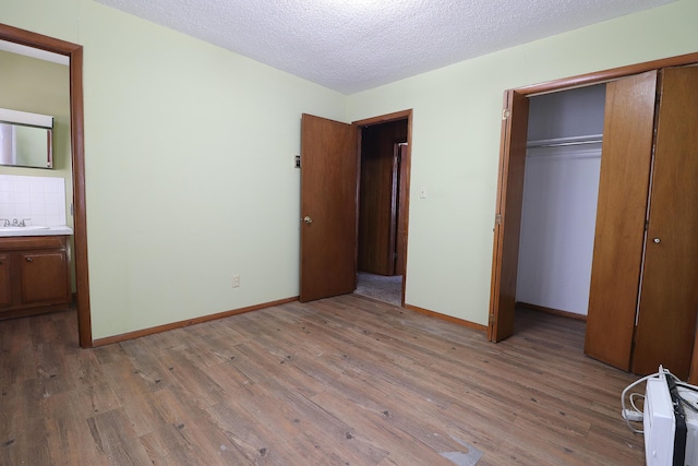 unfurnished bedroom with baseboards, a sink, a textured ceiling, light wood-type flooring, and a closet