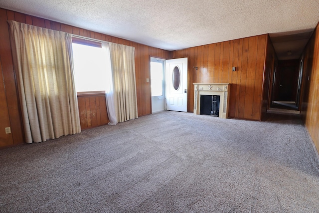 unfurnished living room featuring carpet floors, wood walls, a fireplace, and a textured ceiling