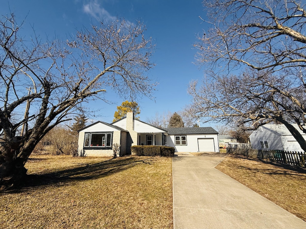 view of front facade featuring a chimney, an attached garage, fence, driveway, and a front lawn