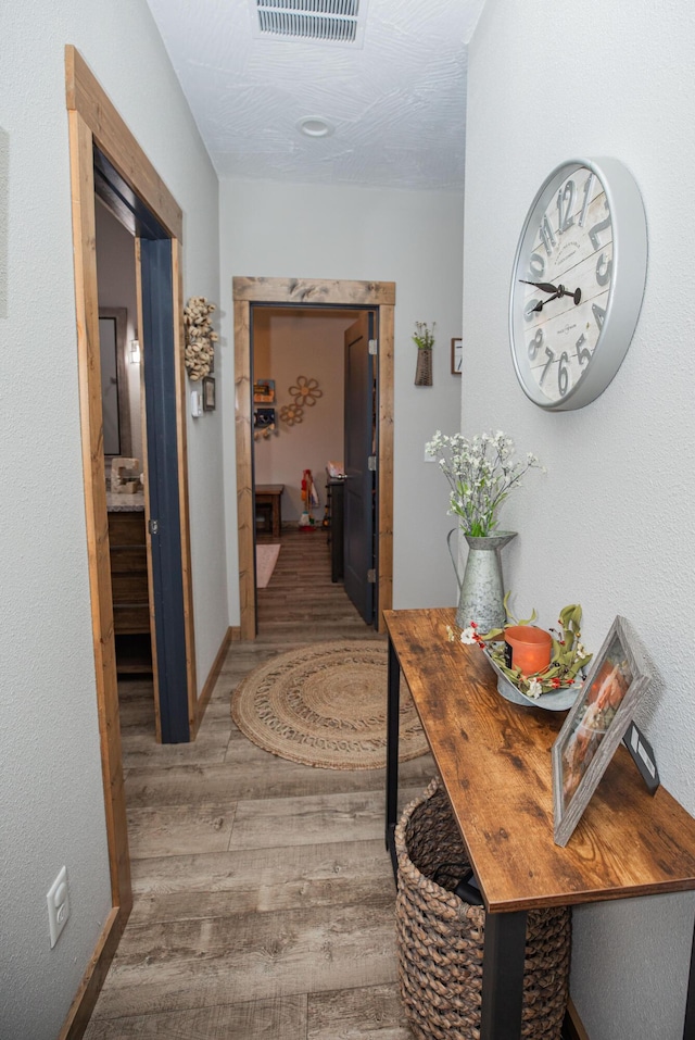 hallway featuring visible vents, baseboards, and wood finished floors